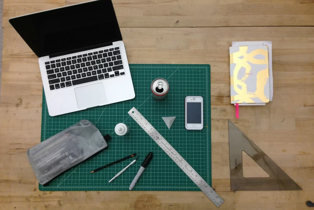 Top-down view of a creative workspace with a laptop, smartphone, ruler, sketchbook, and office tools on a green cutting mat – symbolizing modern office productivity with OffisitePro tools.