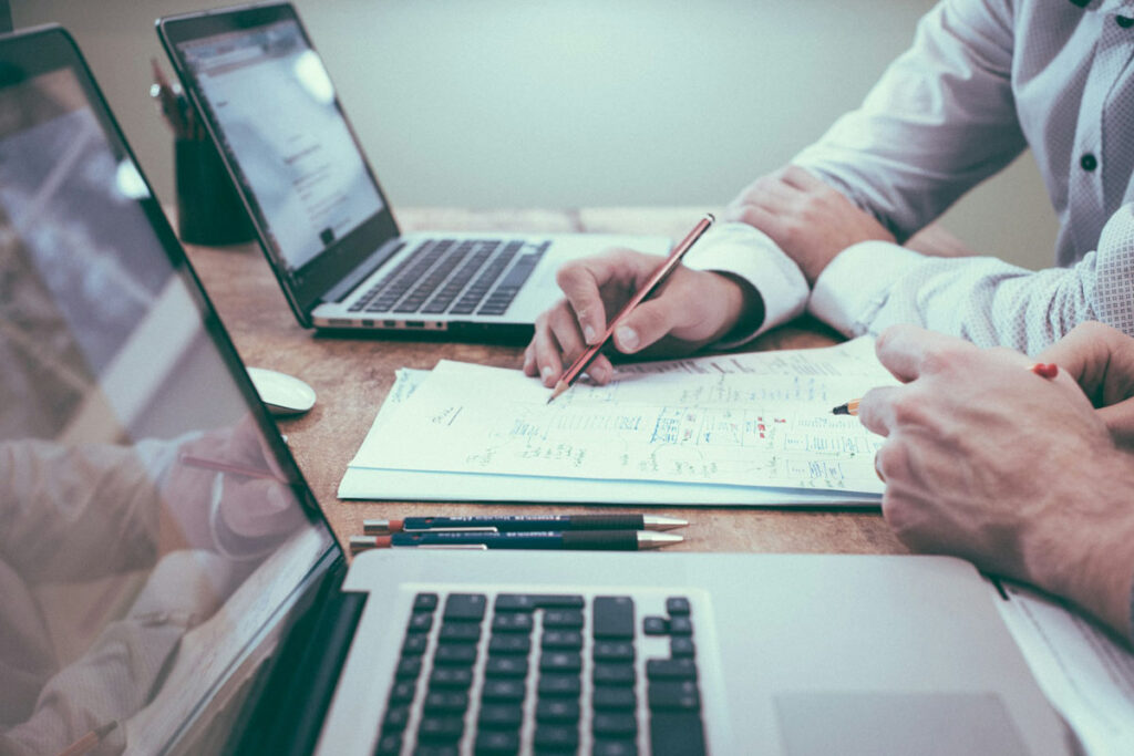 Two professionals collaborating with laptops and documents at a wooden desk, discussing productivity tools – representing OffisitePro’s smart office solutions for 2025.