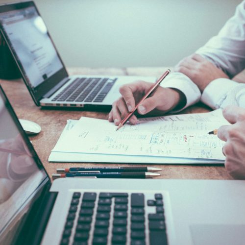 Two professionals collaborating with laptops and documents at a wooden desk, discussing productivity tools – representing OffisitePro’s smart office solutions for 2025.